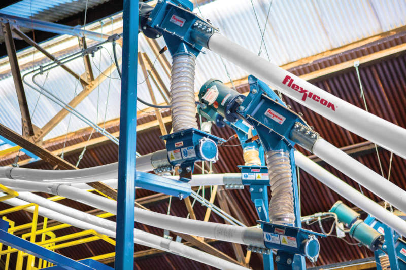 Figure 4: The five topmost flexible screw conveyors empty material into the central weigh hopper above the mixer. Each transition discharge adapter is situated below the drive, avoiding material contact with seals. Courtesy Flexicon Corp.