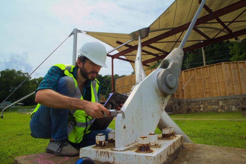 EIT Engineer Stefan Gosey on site using a caliper to measure the thickness of a guy wire anchor plate supporting a tension fabric structure in North Carolina.