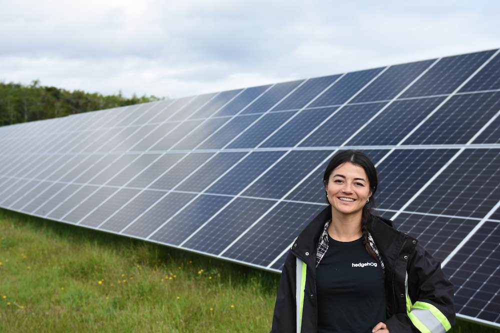 Figure 4: Photo of Hedgehog Technologies' electrical engineer Aileen Maynard standing near a large solar installation. Courtesy: Hedgehog Technologies