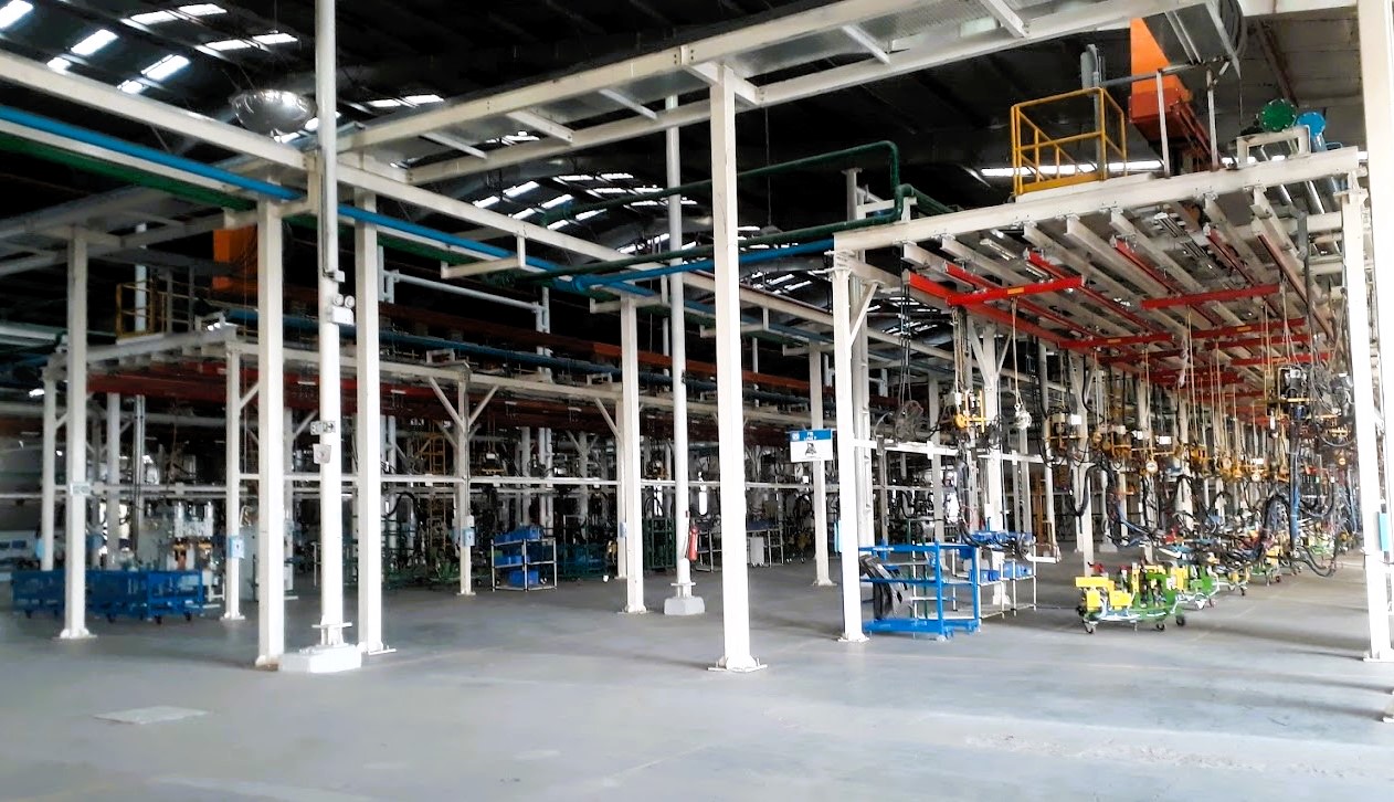 Figure 1: Interior of a large industrial facility with metal beams, pipes, and machinery, featuring a spacious layout and a concrete floor. Courtesy: NEXGEN